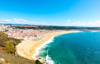 Panoramaudsigt over den gyldne sandstrand i Nazaré, Portugal, med byens farverige tage og det azurblå Atlanterhav