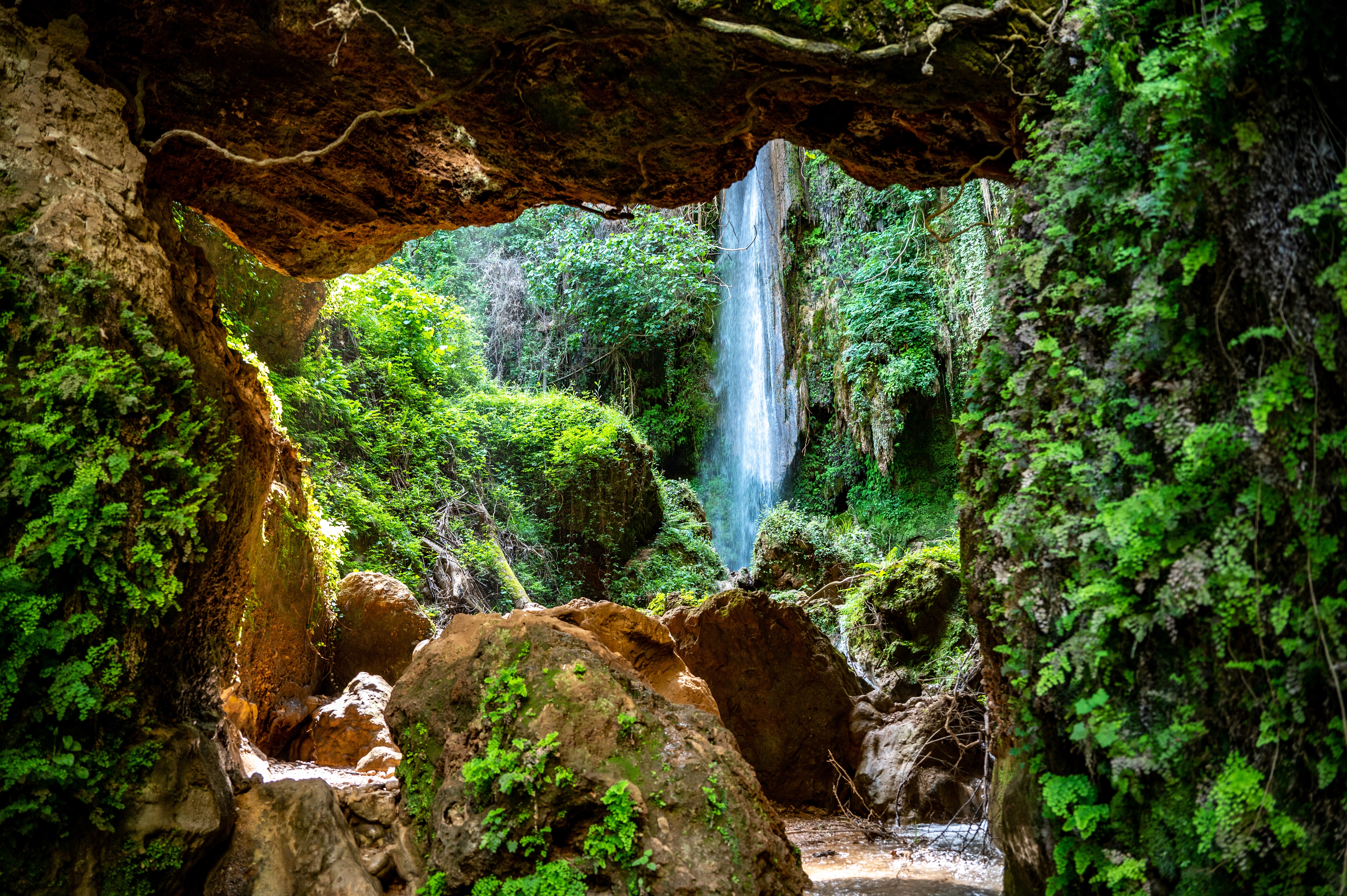Det betagende Nemouta-vandfald i Peloponnes, Grækenland, omgivet af frodig grøn vegetation og en naturlig grotte