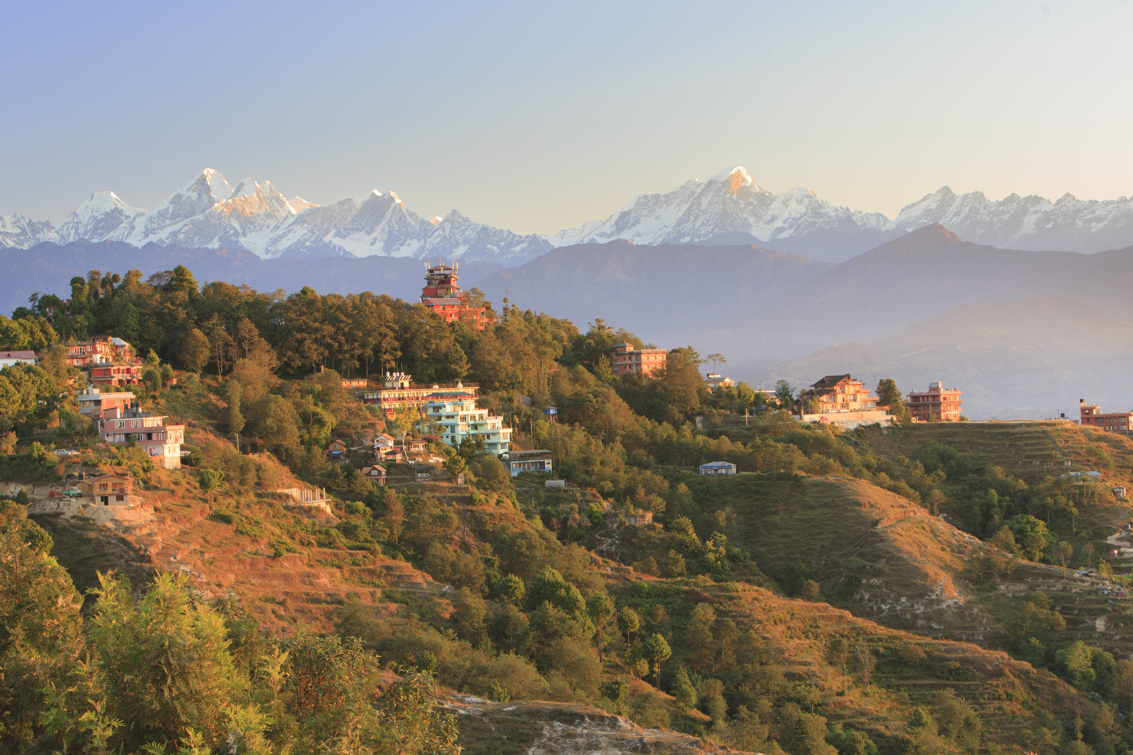 Bjerglandsby i Nepal med traditionelle huse og sne-dækkede Himalaya-toppe i baggrunden
