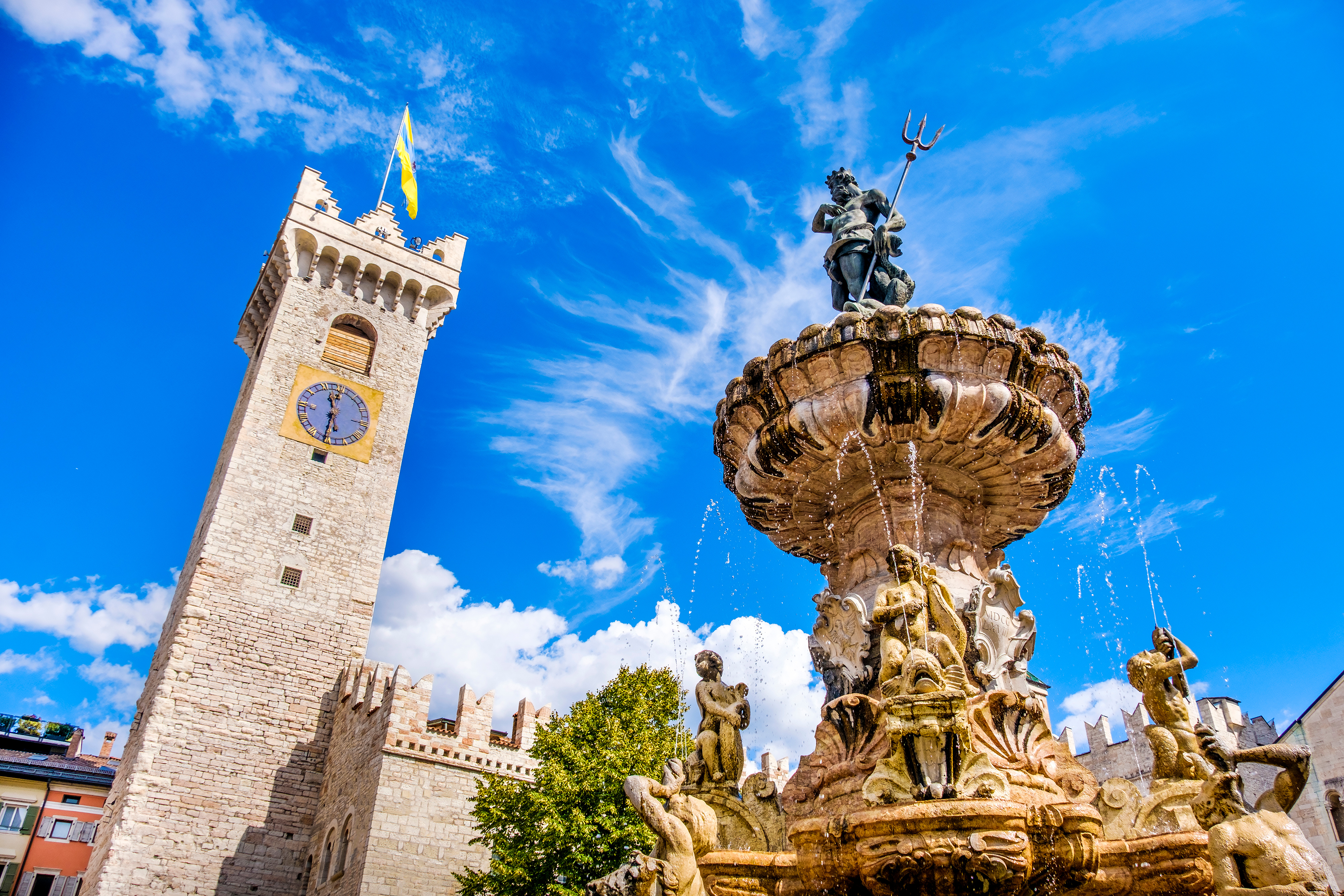 Neptunfontænen og Torre Civica-klokketårnet på Piazza del Duomo i Trento, Italien, under en strålende blå sommerhimmel