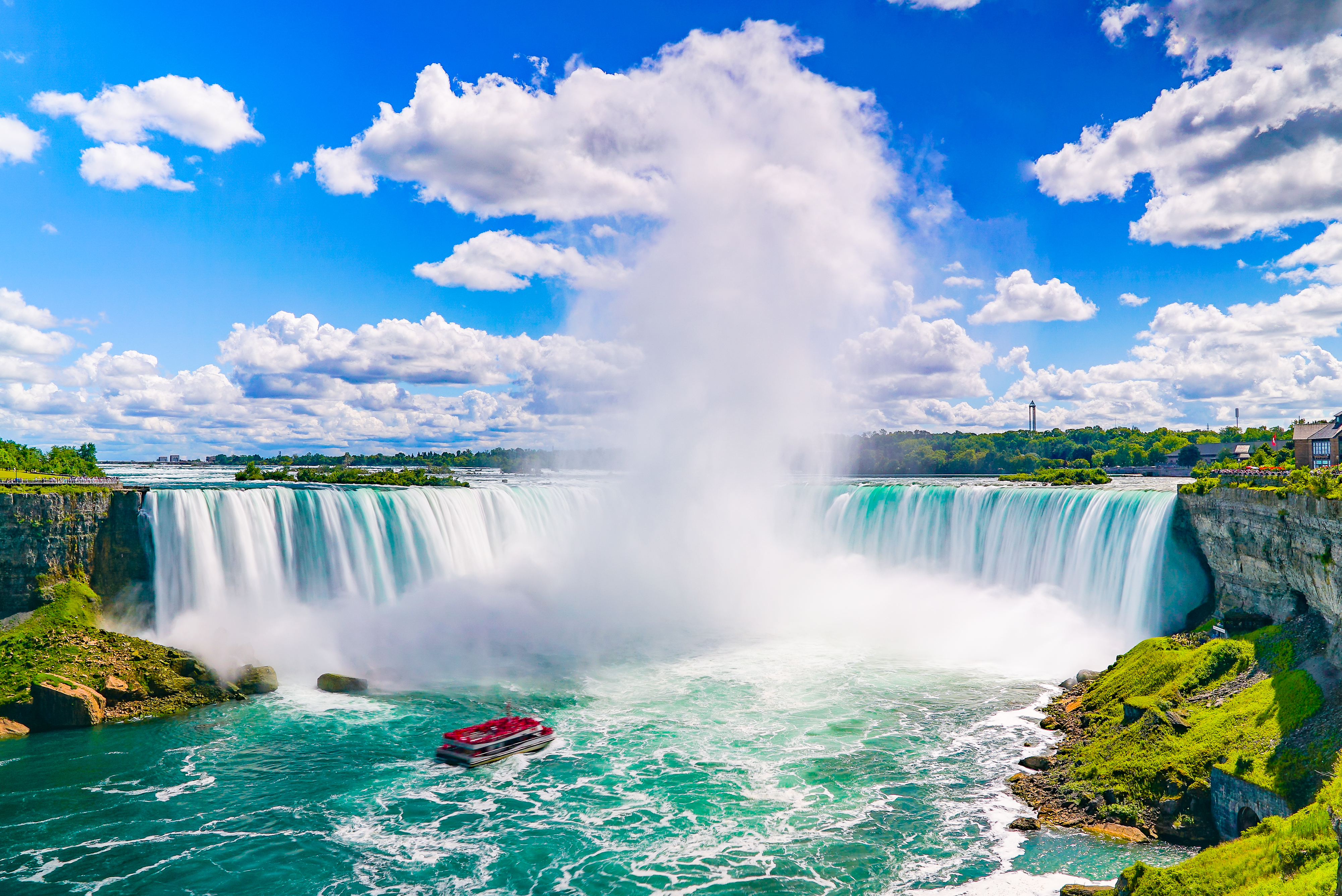Imponerende udsigt over Niagara-vandfaldene med turkisblåt vand, der styrter ned over klipperne med tåge og turistbåd i forgrunden