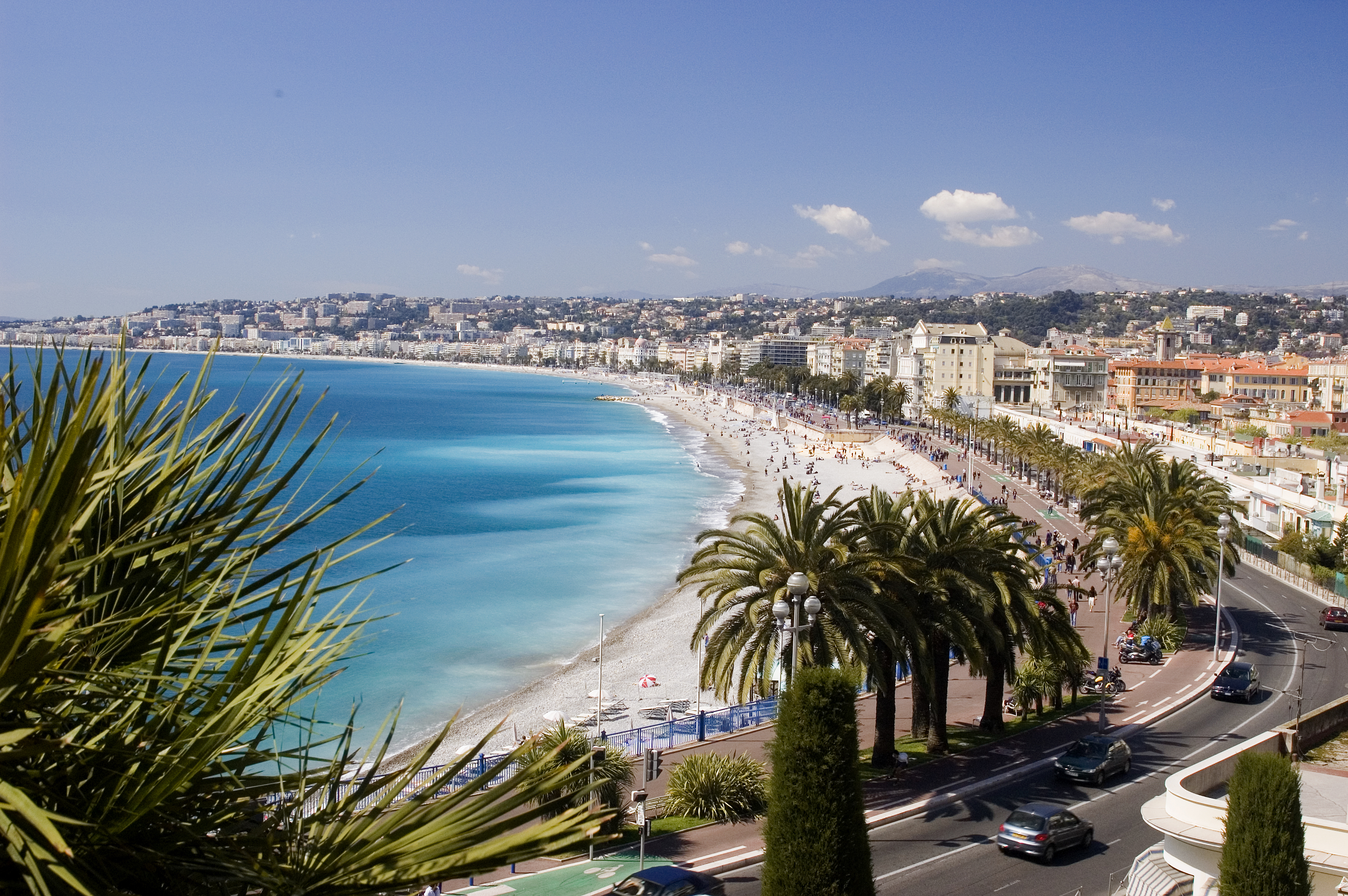 Panoramaudsigt over Nice i Frankrig med turkisblåt Middelhav, sandstrand og palmelinede Promenade des Anglais på den franske riviera
