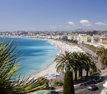 Panoramaudsigt over Nice i Frankrig med turkisblåt Middelhav, sandstrand og palmelinede Promenade des Anglais på den franske riviera