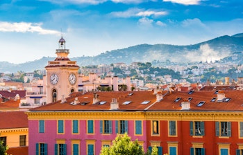 Det historiske urtårn i Port Lympia, der knejser over farverige middelhavsbyggerier i Nice's gamle bydel med azurblå himmel og kystbjerge i baggrunden