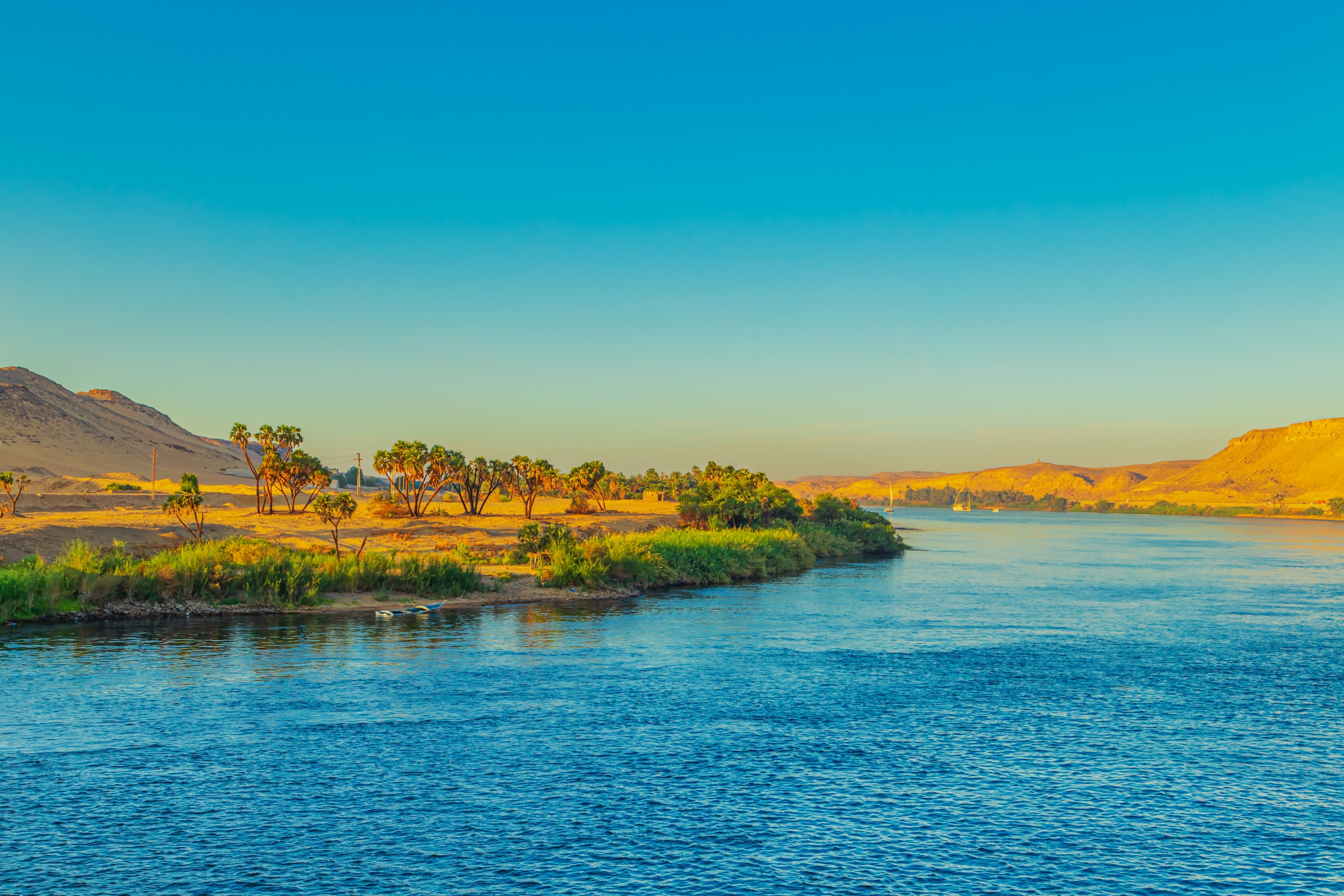 Smuk udsigt over Nilen ved Aswan i Egypten med frodig grøn vegetation langs bredden og gyldent ørkenlandskab i solnedgangen