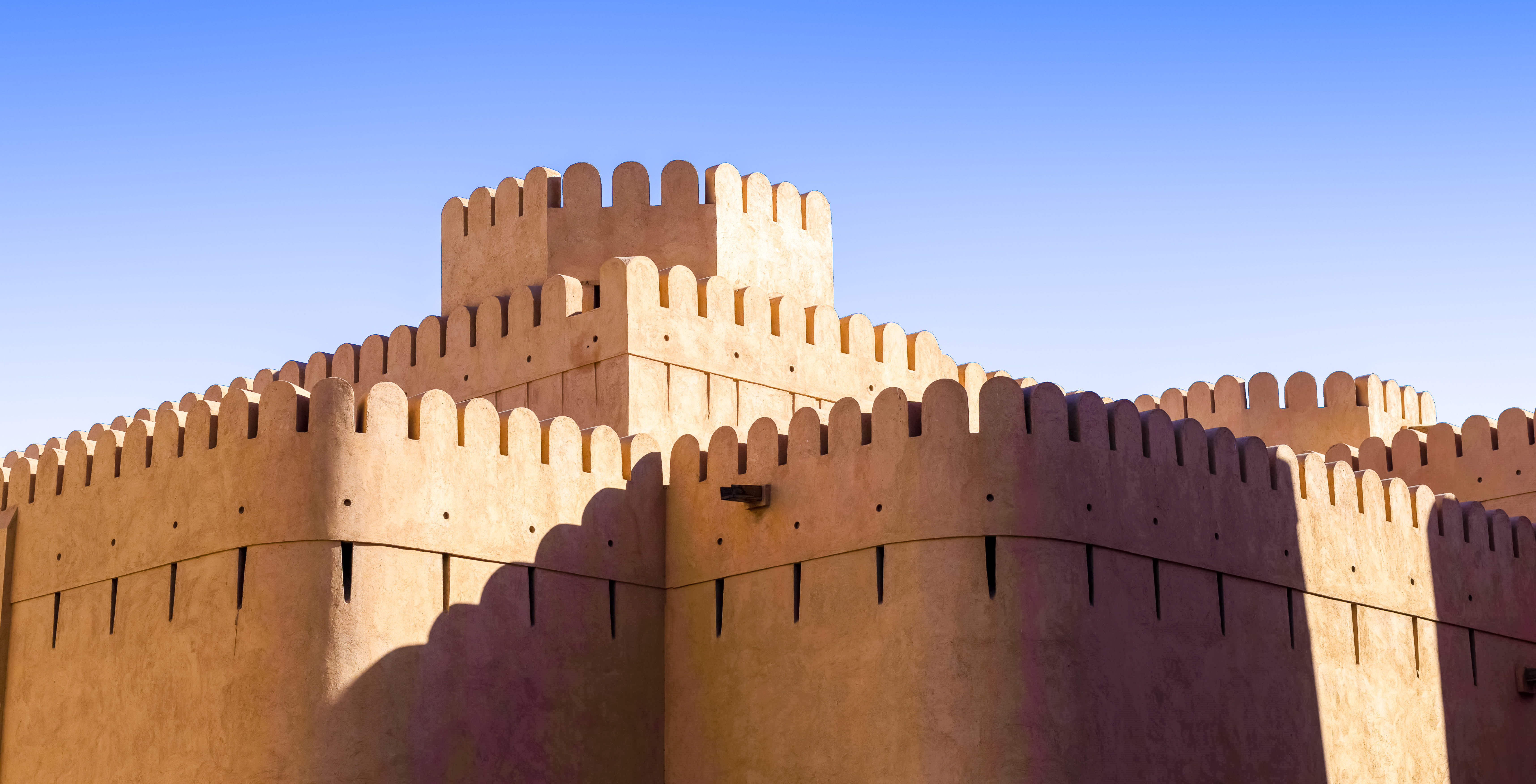 Det historiske Nizwa Fort i Oman med karakteristiske sandfarvet mure og takkede tårne mod den blå himmel, en ikonisk seværdighed på rejser til Mellemøsten