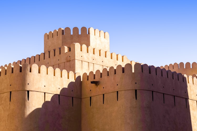 Det historiske Nizwa Fort i Oman med karakteristiske sandfarvet mure og takkede tårne mod den blå himmel, en ikonisk seværdighed på rejser til Mellemøsten