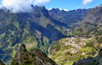 Betagende udsigt over Nonnernes Dal på Madeira med dramatiske bjergtinder, frodige grønne skråninger og en lille landsby omgivet af majestætiske bjerge