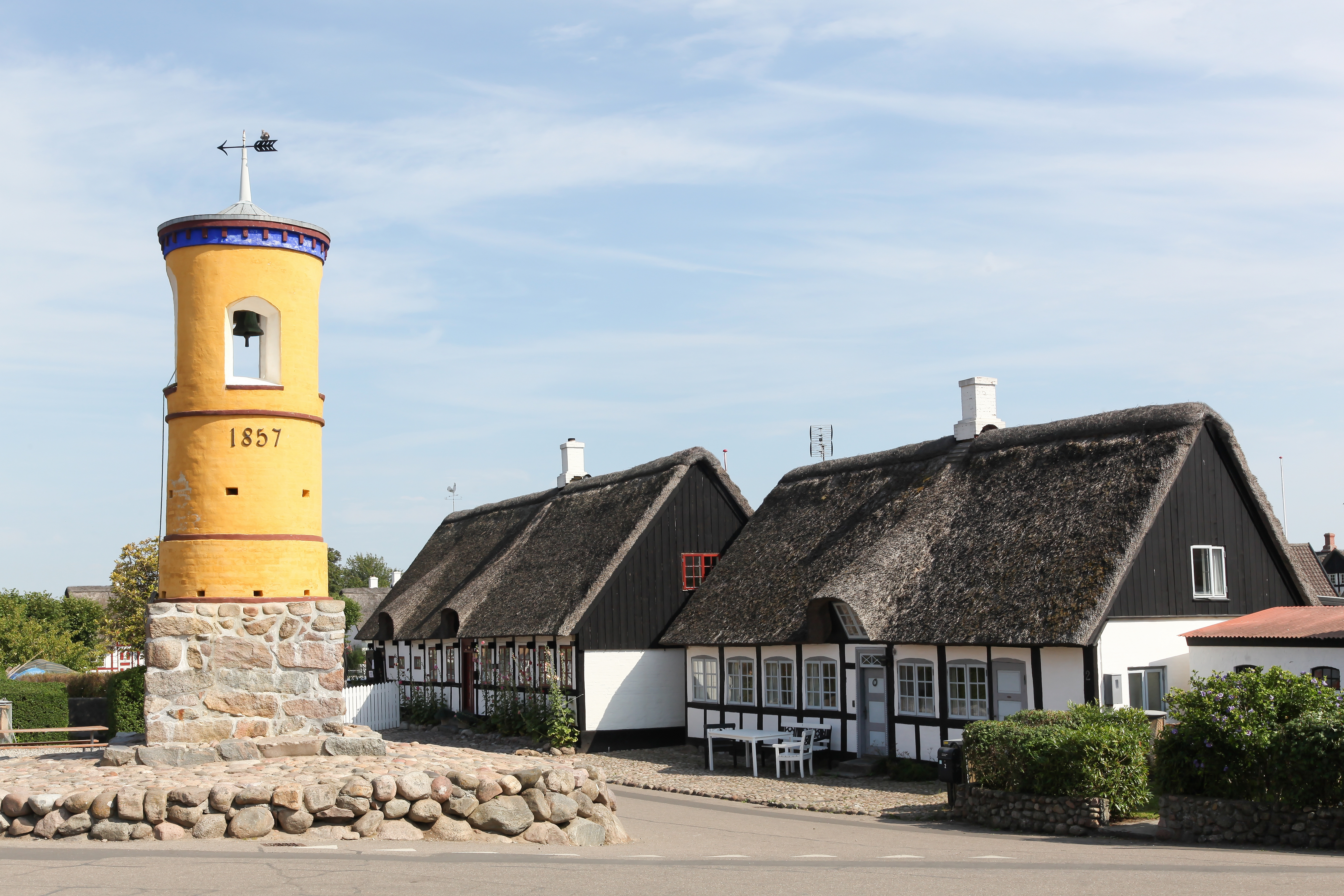 Historisk gult klokketa rn fra 1857 i Nordby på Samsø med traditionelle stråta gte bindingsva rkshuse i baggrunden