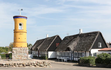 Historisk gult klokketa rn fra 1857 i Nordby på Samsø med traditionelle stråta gte bindingsva rkshuse i baggrunden