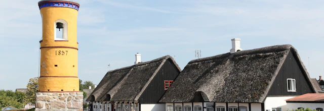Historisk gult klokketa rn fra 1857 i Nordby på Samsø med traditionelle stråta gte bindingsva rkshuse i baggrunden