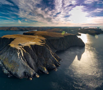 Luftfoto af Nordkap i Norge med dramatiske klipper og gyldent sollys over havet