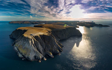 Luftfoto af Nordkap i Norge med dramatiske klipper og gyldent sollys over havet
