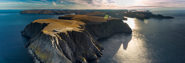 Luftfoto af Nordkap i Norge med dramatiske klipper og gyldent sollys over havet