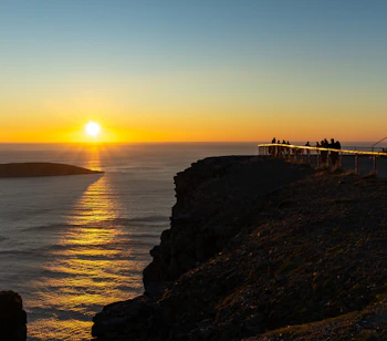 Magisk solnedgang ved Nordkapp i Norge med det ikoniske globus-monument på klippen og den gyldne sol, der spejler sig i Ishavet