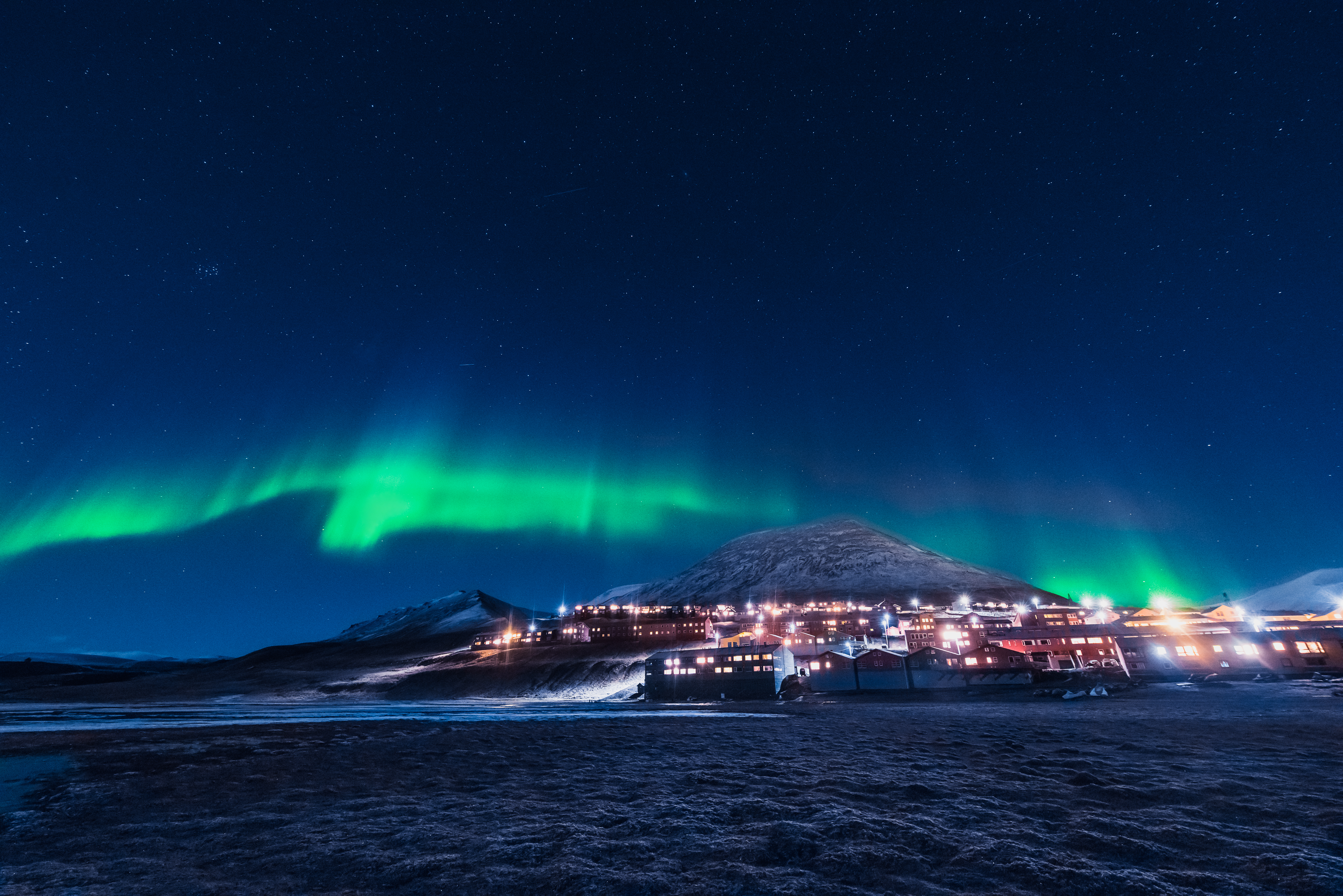 Nordlys og aurora borealis lyser grønt op over den oplyste by Longyearbyen på Svalbard i Norge med snedækkede bjerge og stjerneklar nattehimmel
