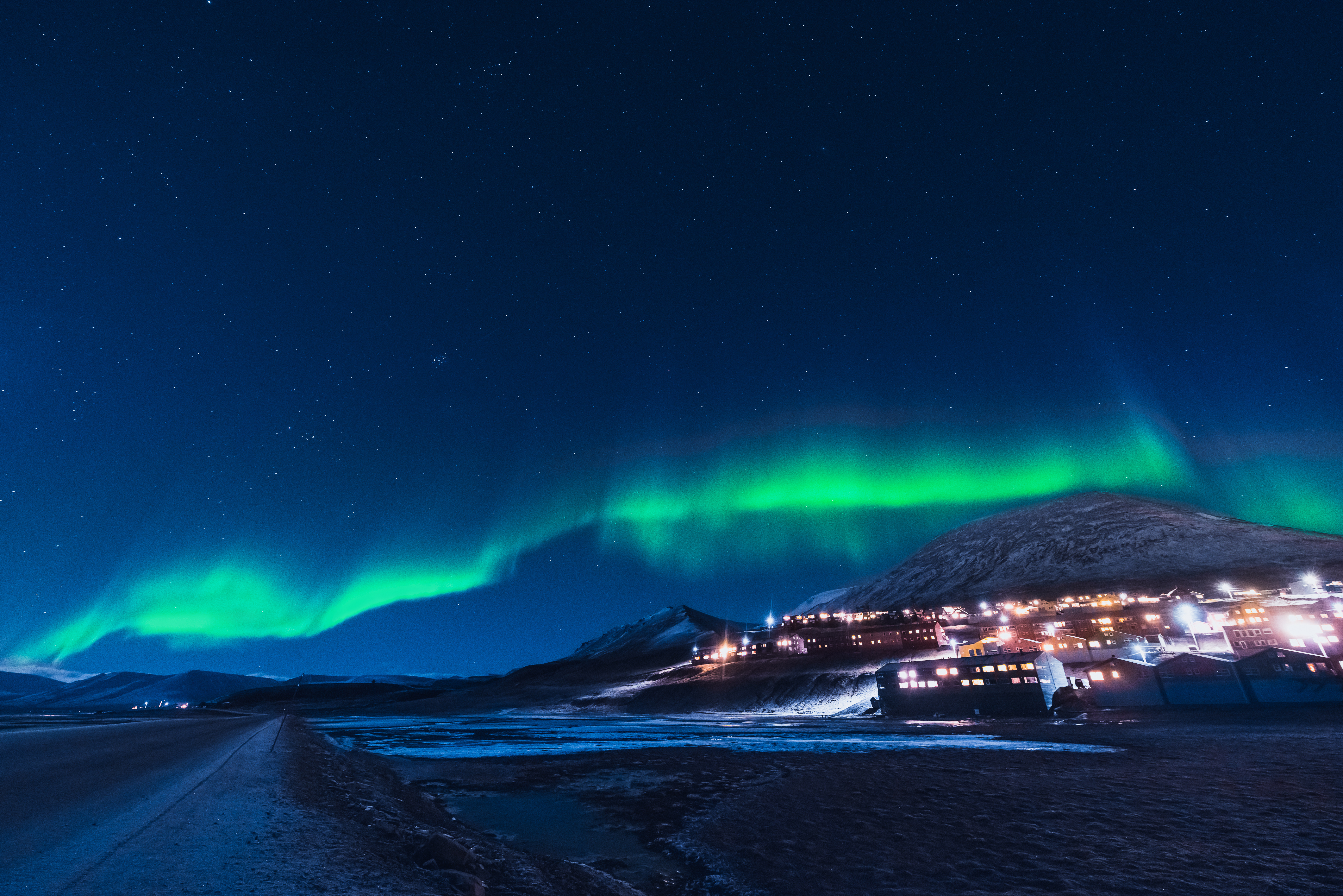 Grønne nordlys over arktisk landsby med sneklædte bjerge under stjerneklar nat