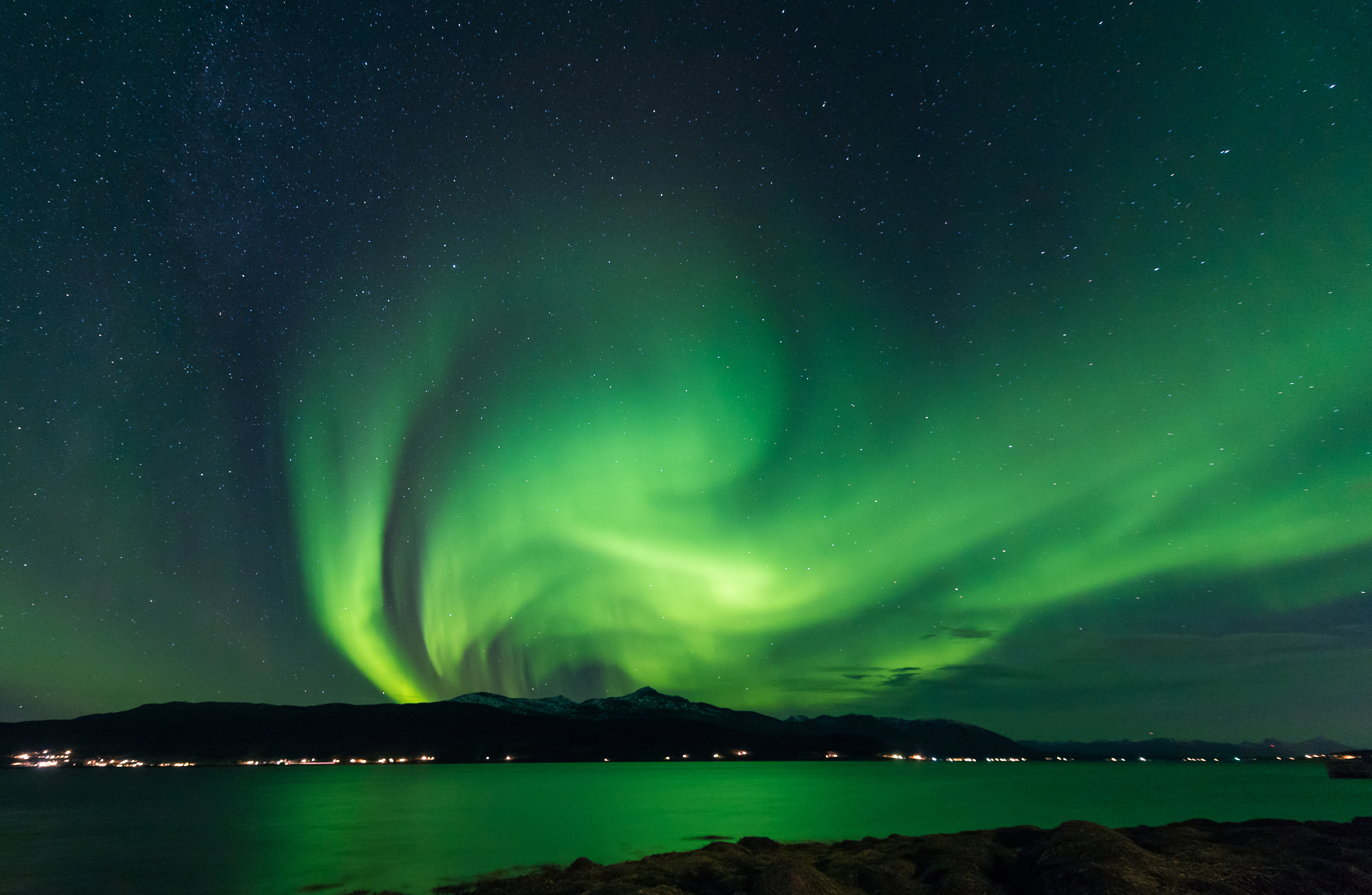 Spektakulært nordlys i grønne nuancer danser over arktisk landskab med stjerneklar himmel og vandspejling