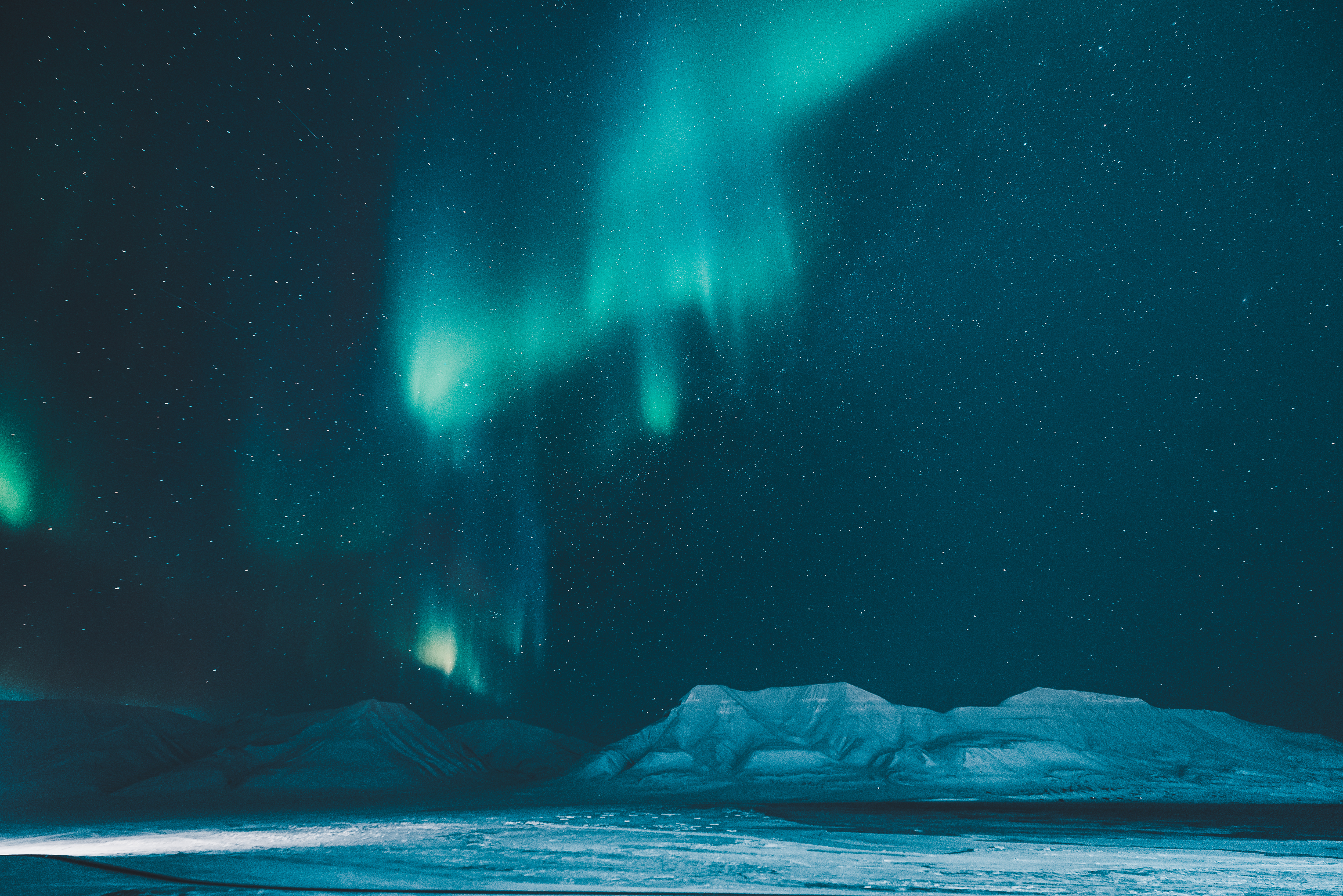 Nordlys over snedækket arktisk landskab med bjerge under stjerneklar himmel
