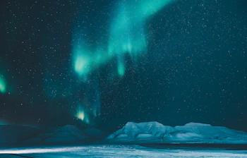 Nordlys over snedækket arktisk landskab med bjerge under stjerneklar himmel