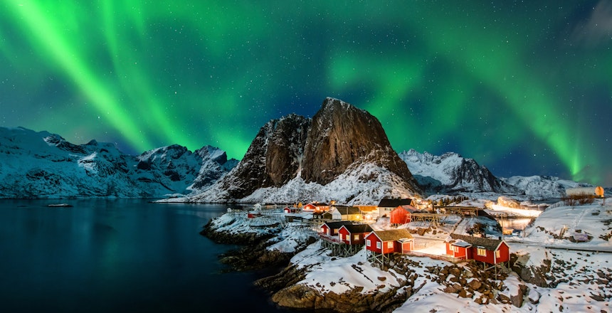 Magisk nordlys danser over de traditionelle røde fiskerhuse i Hamnøy, Lofoten, Norge på en klar vinteraften
