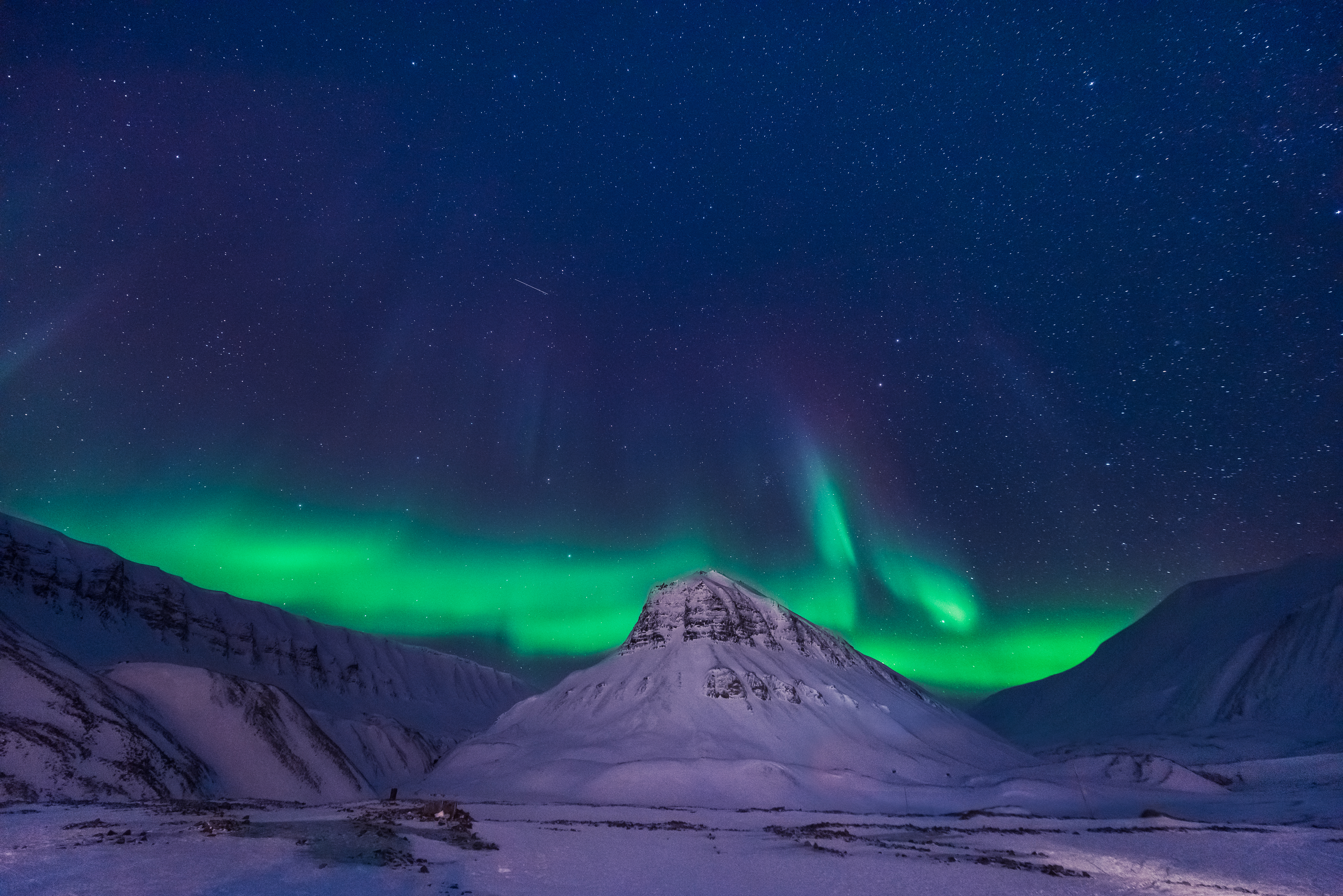 Spektakulært nordlys danser over snedækkede bjerge i arktisk landskab under stjerneklar himmel