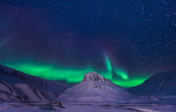 Spektakulært nordlys danser over snedækkede bjerge i arktisk landskab under stjerneklar himmel