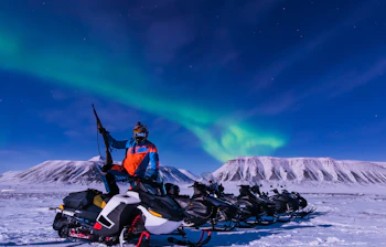 Snescooterrejse under det magiske nordlys ved snedækkede bjerge i Svalbard, Longyearbyen, Norge