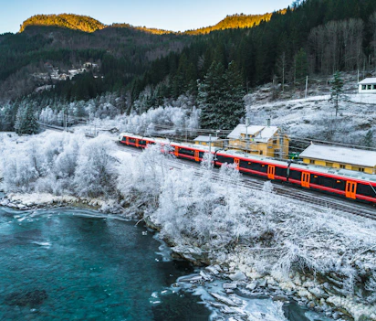 Rødt norsk tog kører gennem sneklædt vinterlandskab med rimfrostdækkede træer og turkis flod