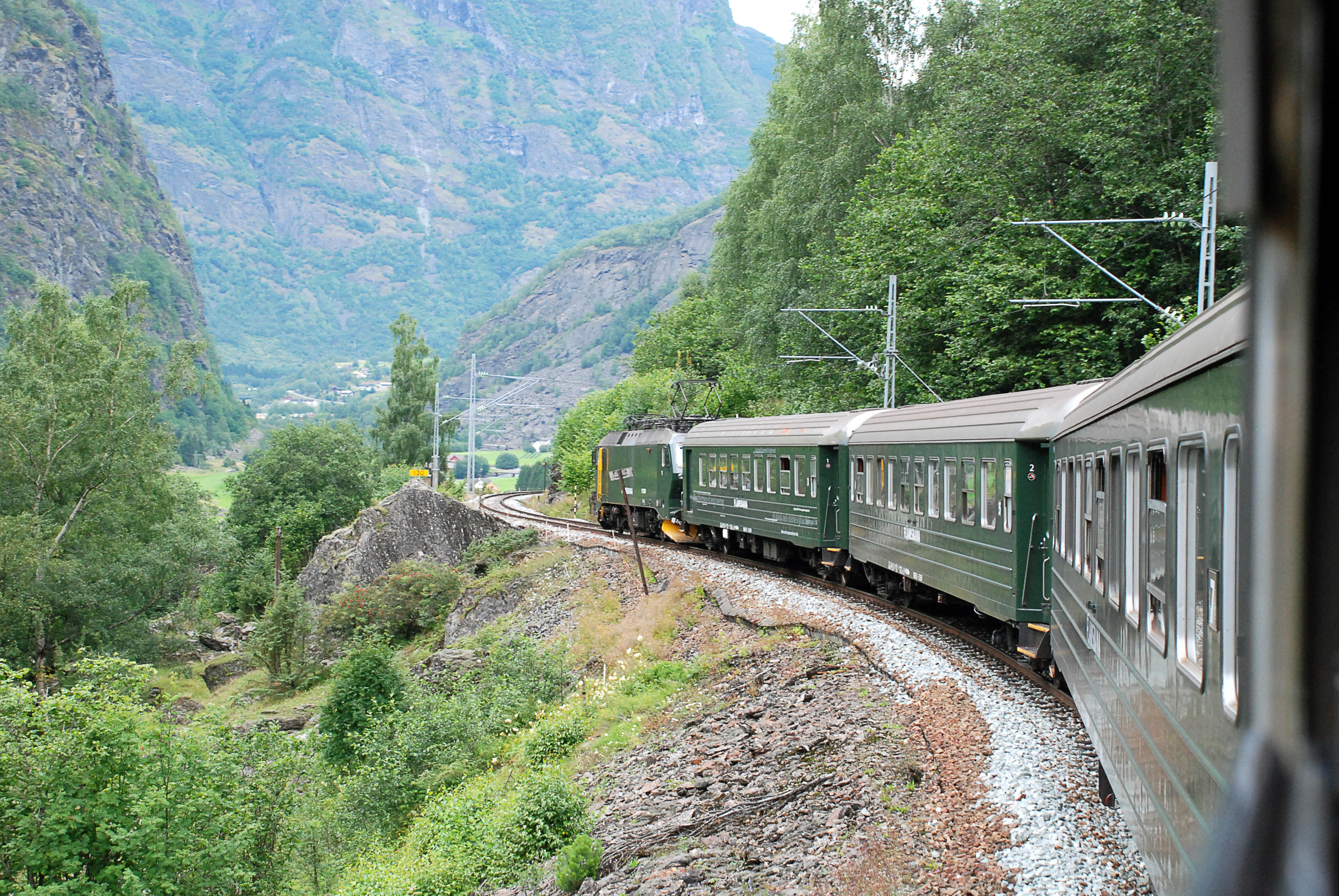 Malerisk togrejse gennem norsk fjordlandskab med groenne bjerge og traditionelle togvogne