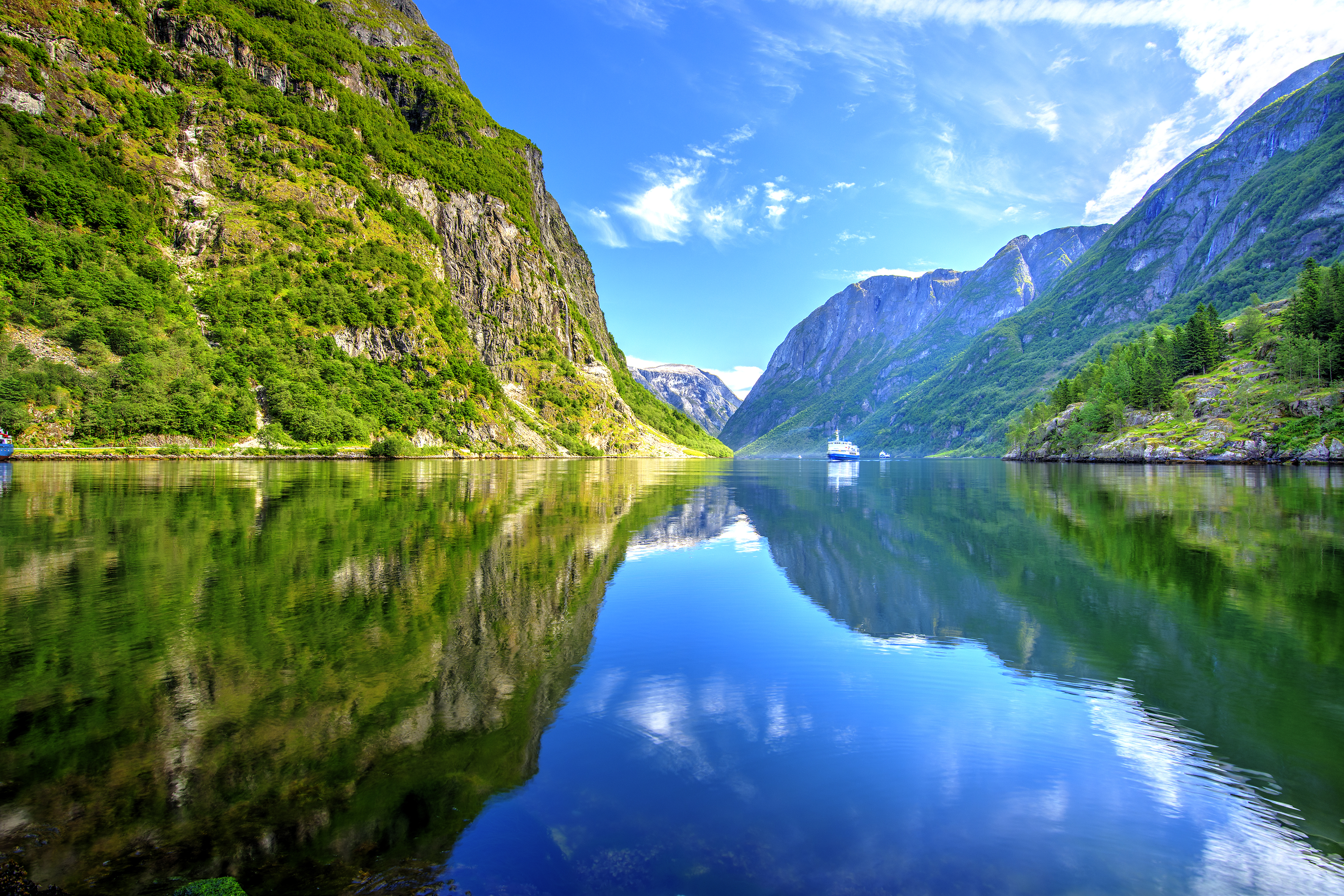 Spektakulære norske fjorde med spejlblankt vand, grønne bjerge og krydstogtskib sejlende gennem naturskønt landskab