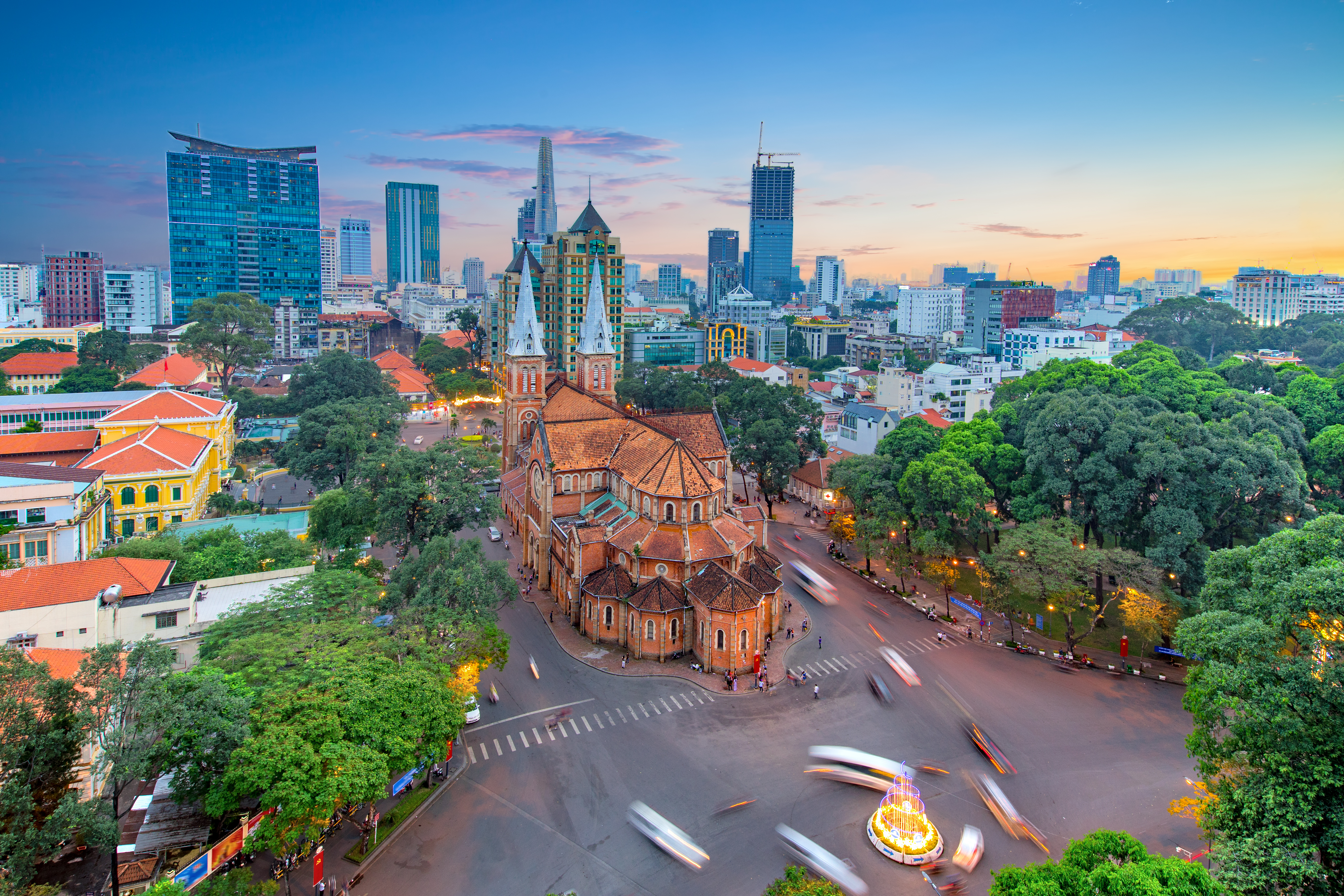 Luftfoto af Notre-Dame Katedralen i Saigon ved tusmørke med Ho Chi Minh Citys skyline i baggrunden, Vietnam