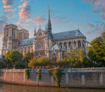 Den ikoniske Notre Dame-katedral i Paris badet i gyldent solnedgangslys, set fra Seinen med sin majestætiske gotiske arkitektur