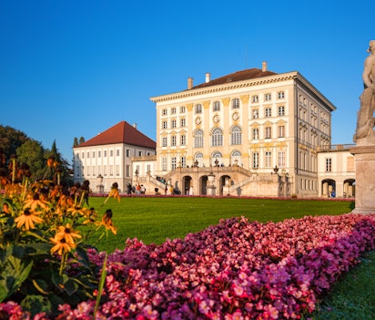 Det imponerende Nymphenburg Slot i München med dets barokke arkitektur spejlet i den ornamentale kanal, omgivet af veltrimmede haver under en klar blå himmel