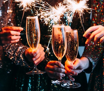 Tre personer fejrer nytår med champagne og stjernekastere i elegante glimmerkjoler