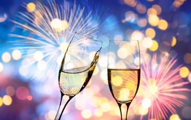 Champagneglas der skåler mod festligt nytårsfyrværkeri med gyldne lys, perfekt til nytårsfejring på rejsen