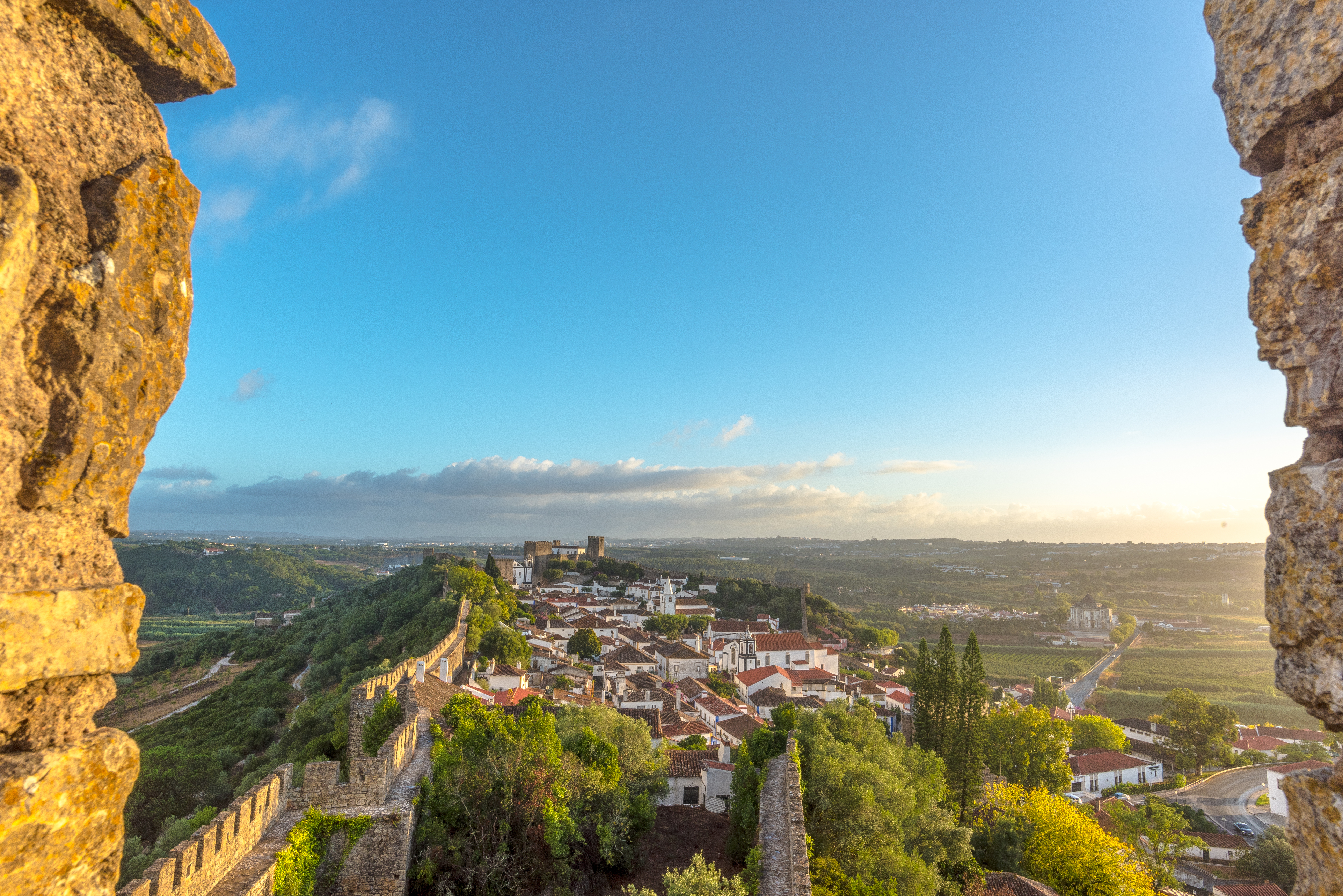 Charmerende udsigt over Óbidos' middelalderlige bylandskab med traditionelle huse, teglstenstage og det historiske Albarra-tårn, der rejser sig over de gamle bymure
