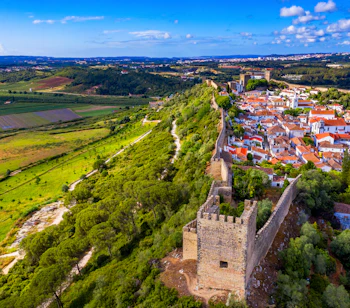 Luftfoto af den middelalderlige befæstede by Óbidos i Portugal med røde tegltage, gamle fæstningstårne og grønt landskab under en blå sommerhimmel