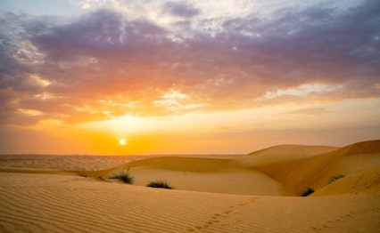 Magisk solopgang over gyldne sanddyner i Mellemøstens ørken med dramatisk orange himmel