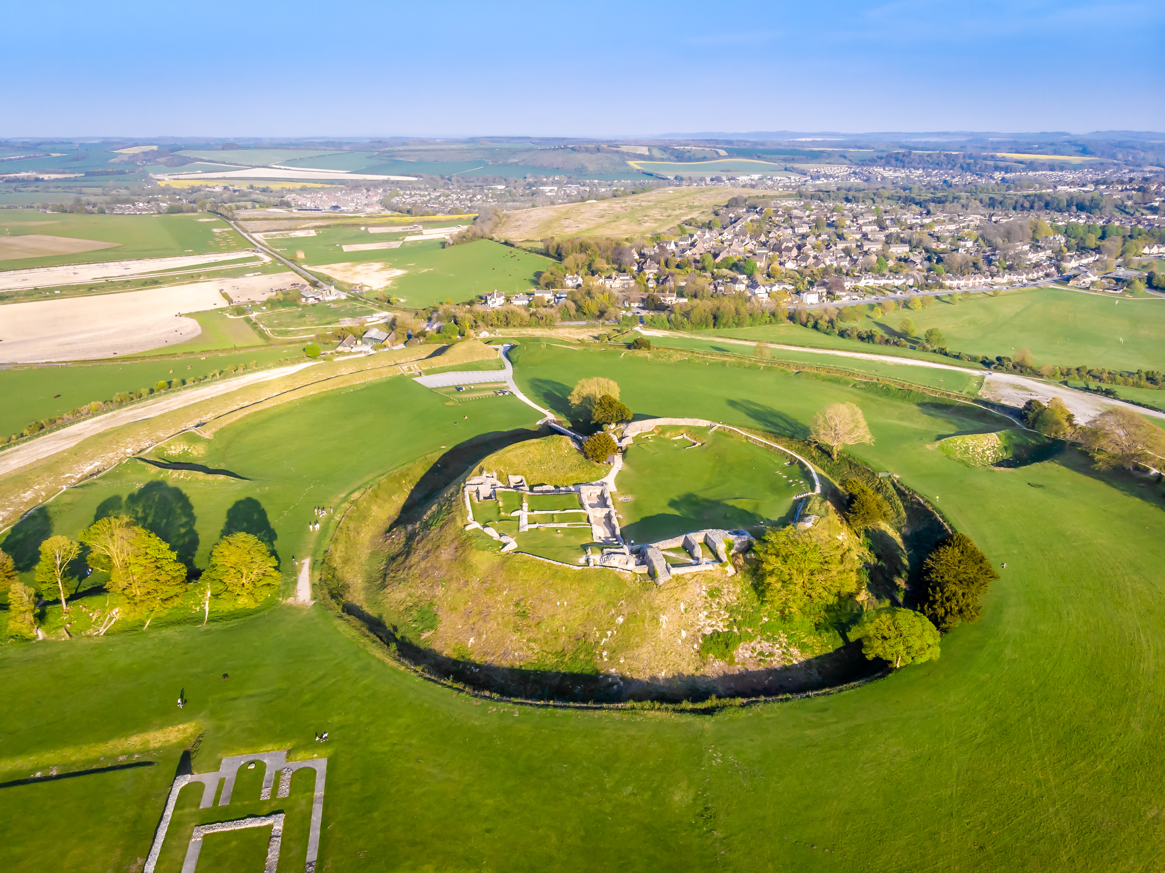 Luftfoto af de historiske ruiner af Old Sarum omgivet af grønne marker i Wiltshire, England.