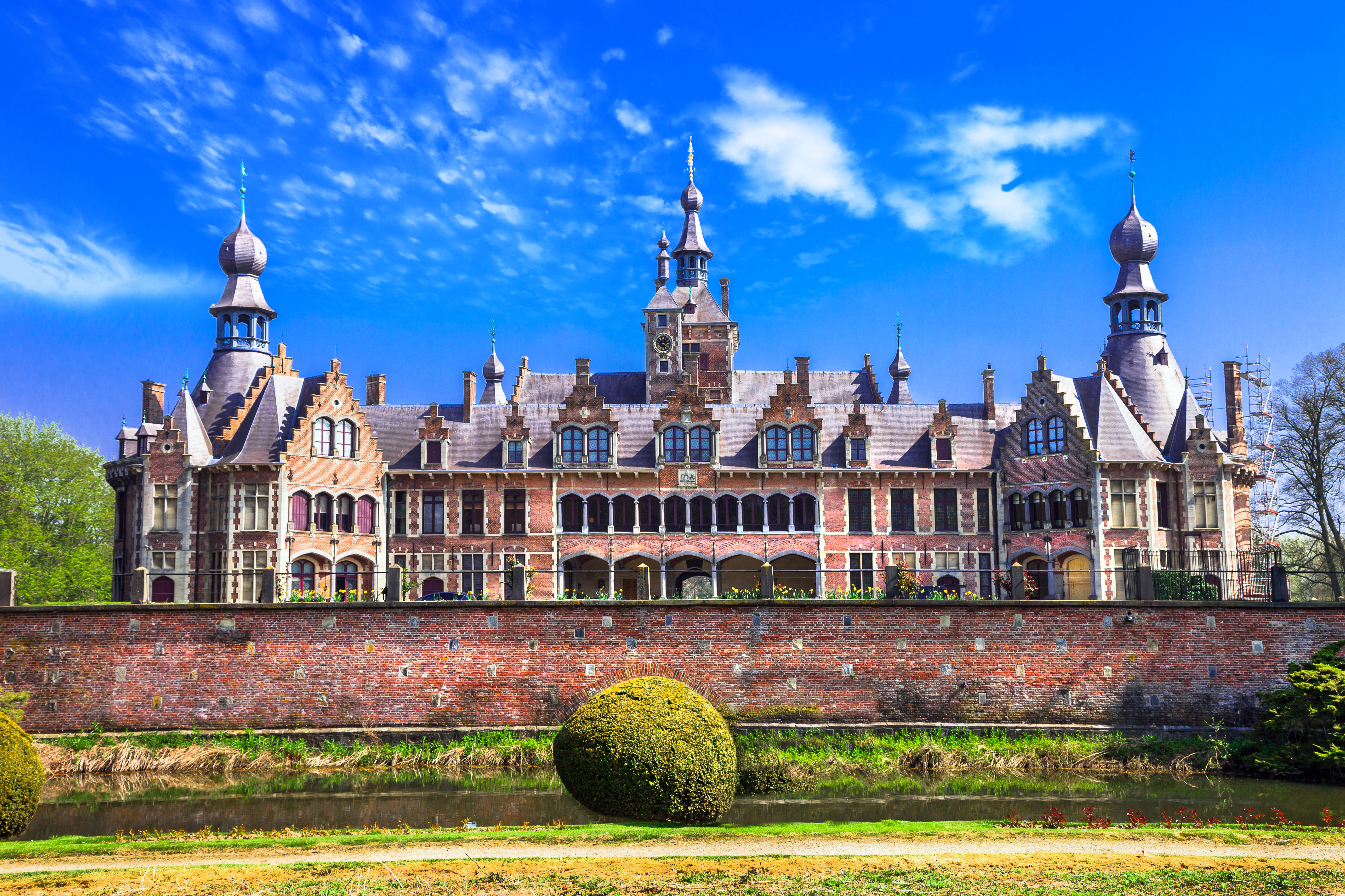 Det eventyrlige Ooidonk Slot i Østflandern, Belgien, med sine imponerende tårne og gotisk arkitektur omgivet af frodige grønne områder under en klar blå sommerhimmel