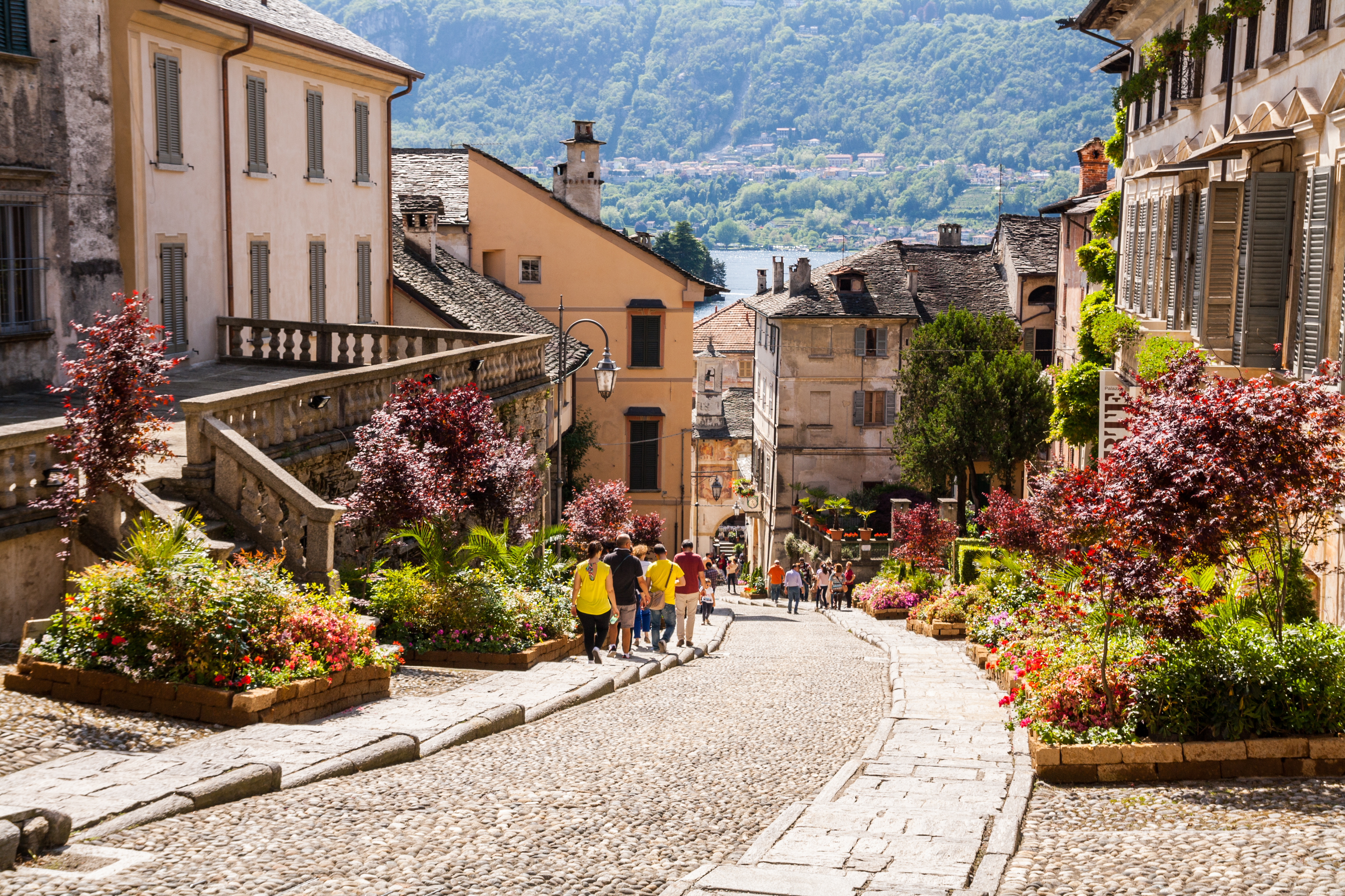 Idyllisk brostensbelagt gade med farverige blomster i det historiske centrum af Orta San Giulio ved Orta-søen