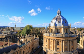 Panoramaudsigt over Oxford Universitet med den ikoniske Radcliffe Camera kuppel og historiske kollegiebygninger set fra St. Mary's kirketårn på en solrig dag