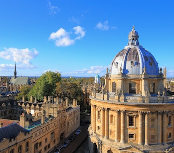 Panoramaudsigt over Oxford Universitet med den ikoniske Radcliffe Camera kuppel og historiske kollegiebygninger set fra St. Mary's kirketårn på en solrig dag