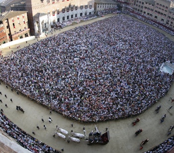 Storslået panoramaudsigt over det historiske Palio-hesteløb på Piazza del Campo i Siena, hvor tusindvis af tilskuere fylder den middelalderlige plads i Toscana