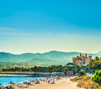 Gylden sandstrand i Palma de Mallorca med badegæster og den majestætiske katedral i baggrunden
