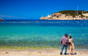 Par nyder den smukke udsigt over havnen i Port de Soller på Mallorca med turkisblåt vand og bjerge i baggrunden