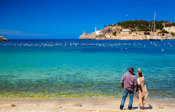 Par nyder den smukke udsigt over havnen i Port de Soller på Mallorca med turkisblåt vand og bjerge i baggrunden