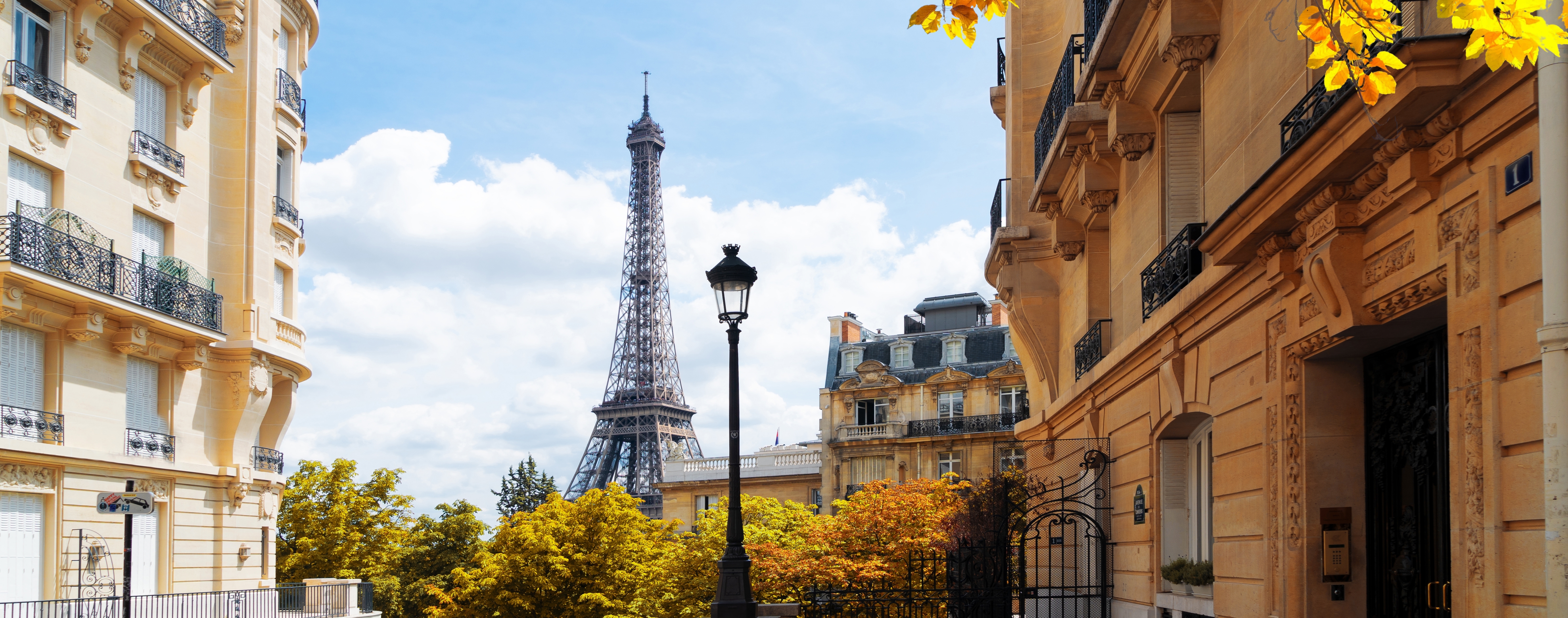 Klassisk parisisk gade med det ikoniske Eiffeltårn synligt over elegante Haussmann-bygninger omgivet af gyldent efterårsblade i Paris, Frankrig