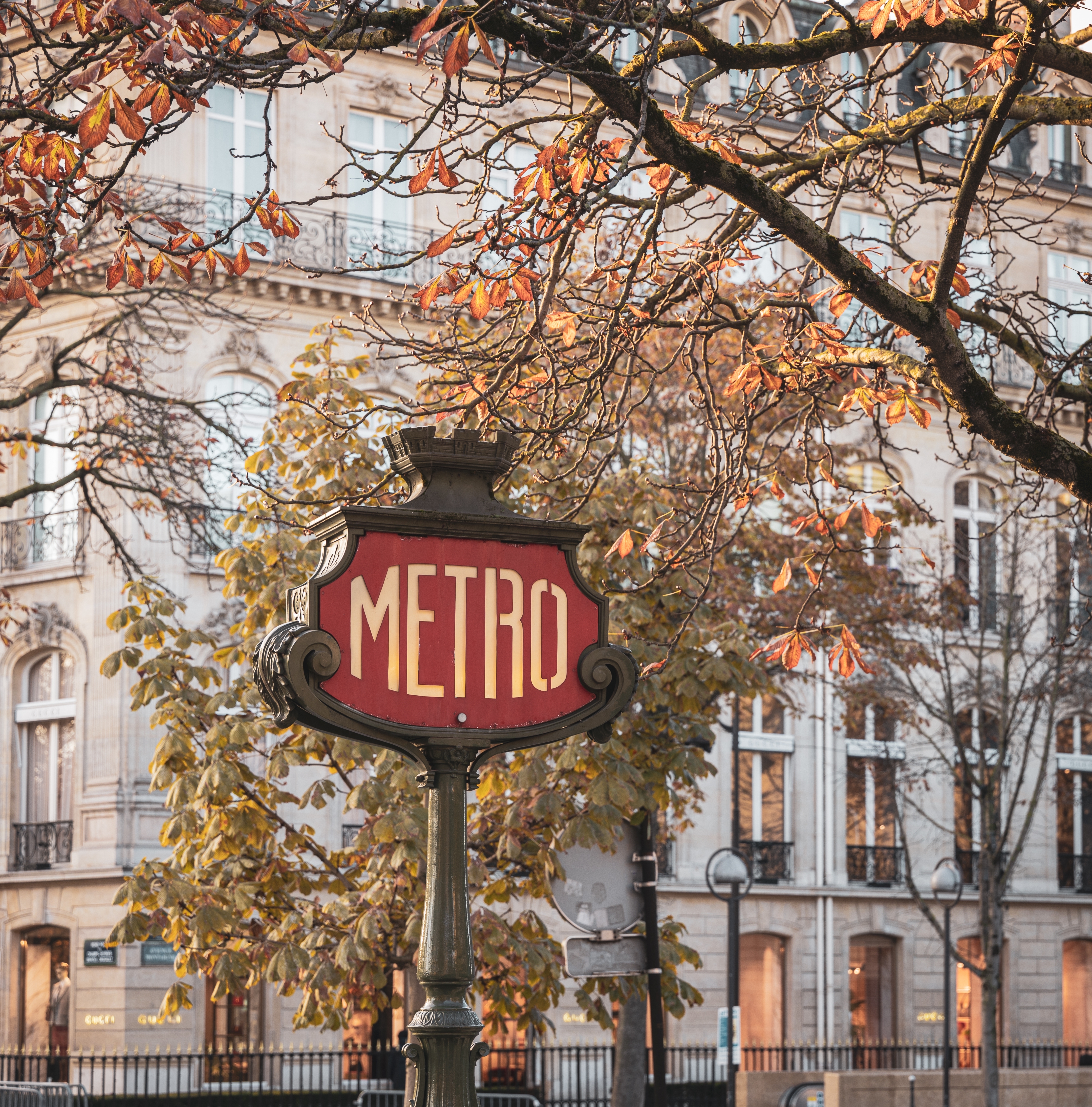 Klassisk Paris Metro skilt i jugendstil omgivet af efterårstræer og smuk haussmannsk bygning i baggrunden, Paris, Frankrig